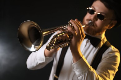 Photo of Professional musician playing trumpet on black background in color lights, selective focus