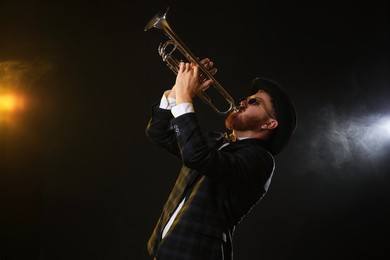 Photo of Professional musician playing trumpet on black background in color lights and smoke