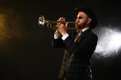 Photo of Professional musician playing trumpet on black background in color lights and smoke. Space for text