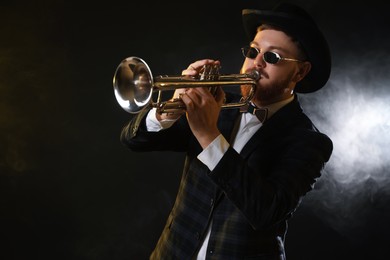 Professional musician playing trumpet on black background in smoke