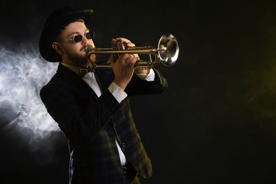 Professional musician playing trumpet on black background in smoke. Space for text