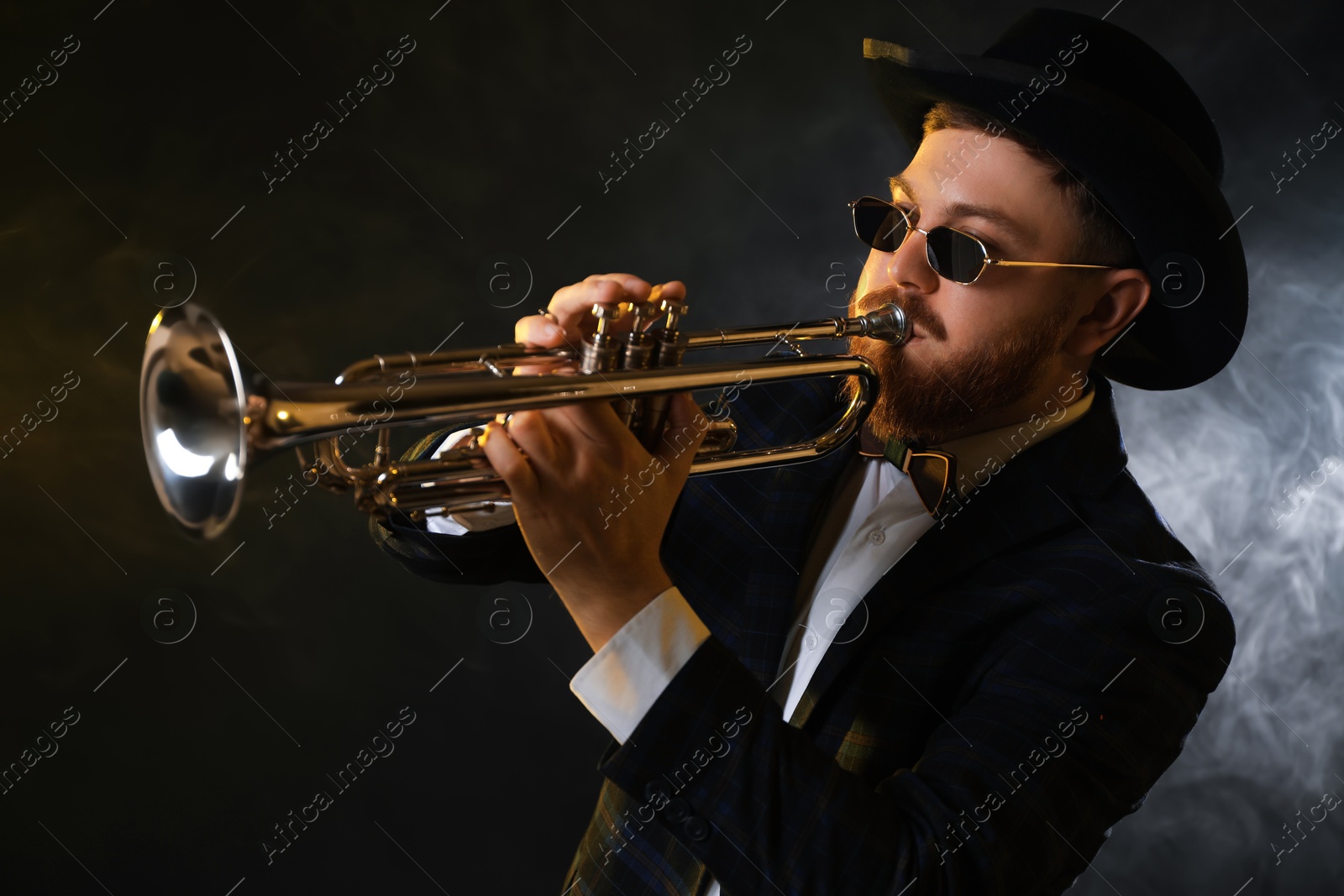 Photo of Professional musician playing trumpet on black background in smoke