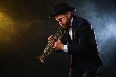 Photo of Professional musician playing trumpet on black background in color lights and smoke. Space for text