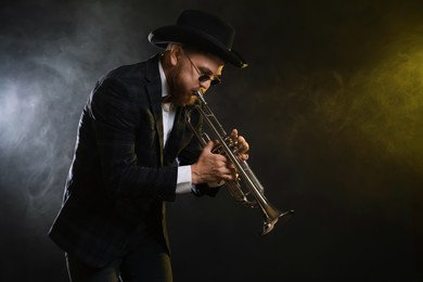 Photo of Professional musician playing trumpet on black background in color lights and smoke. Space for text