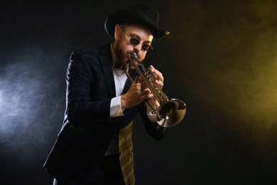 Photo of Professional musician playing trumpet on black background in color lights and smoke. Space for text