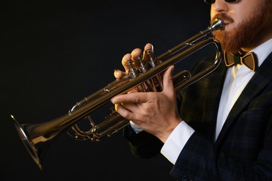 Professional musician playing trumpet on black background, closeup