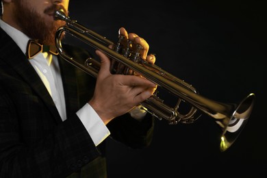 Professional musician playing trumpet on black background, closeup