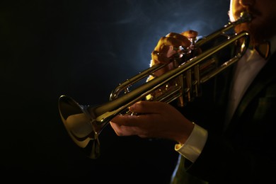 Photo of Professional musician playing trumpet on black background, closeup