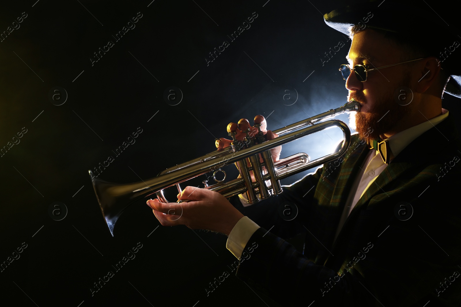 Photo of Professional musician playing trumpet on black background in smoke