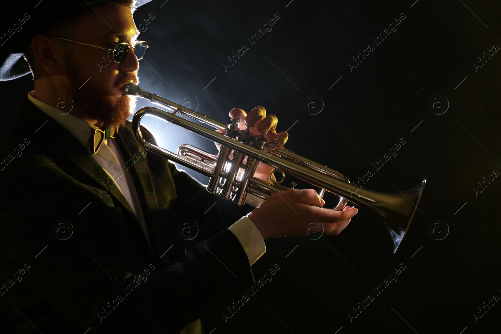 Photo of Professional musician playing trumpet on black background in smoke