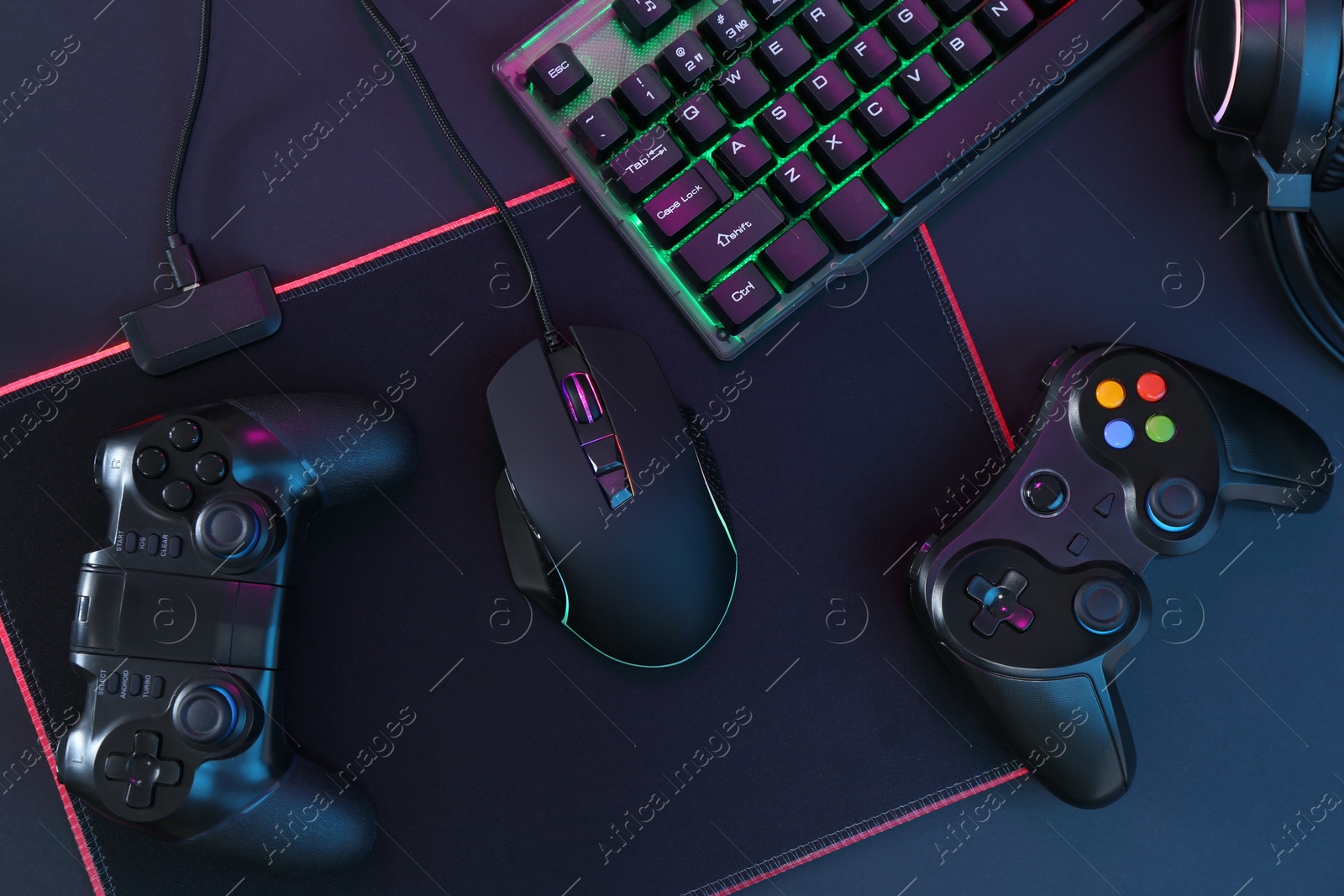 Photo of Computer mouse, RGB keyboard and game controllers on black background, top view