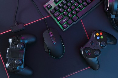 Photo of Computer mouse, RGB keyboard and game controllers on black background, top view