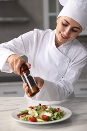 Photo of Professional chef adding pepper to delicious salad at white marble table in kitchen