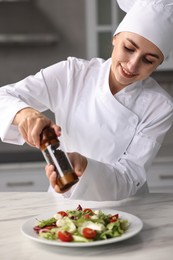 Professional chef adding pepper to delicious salad at white marble table in kitchen