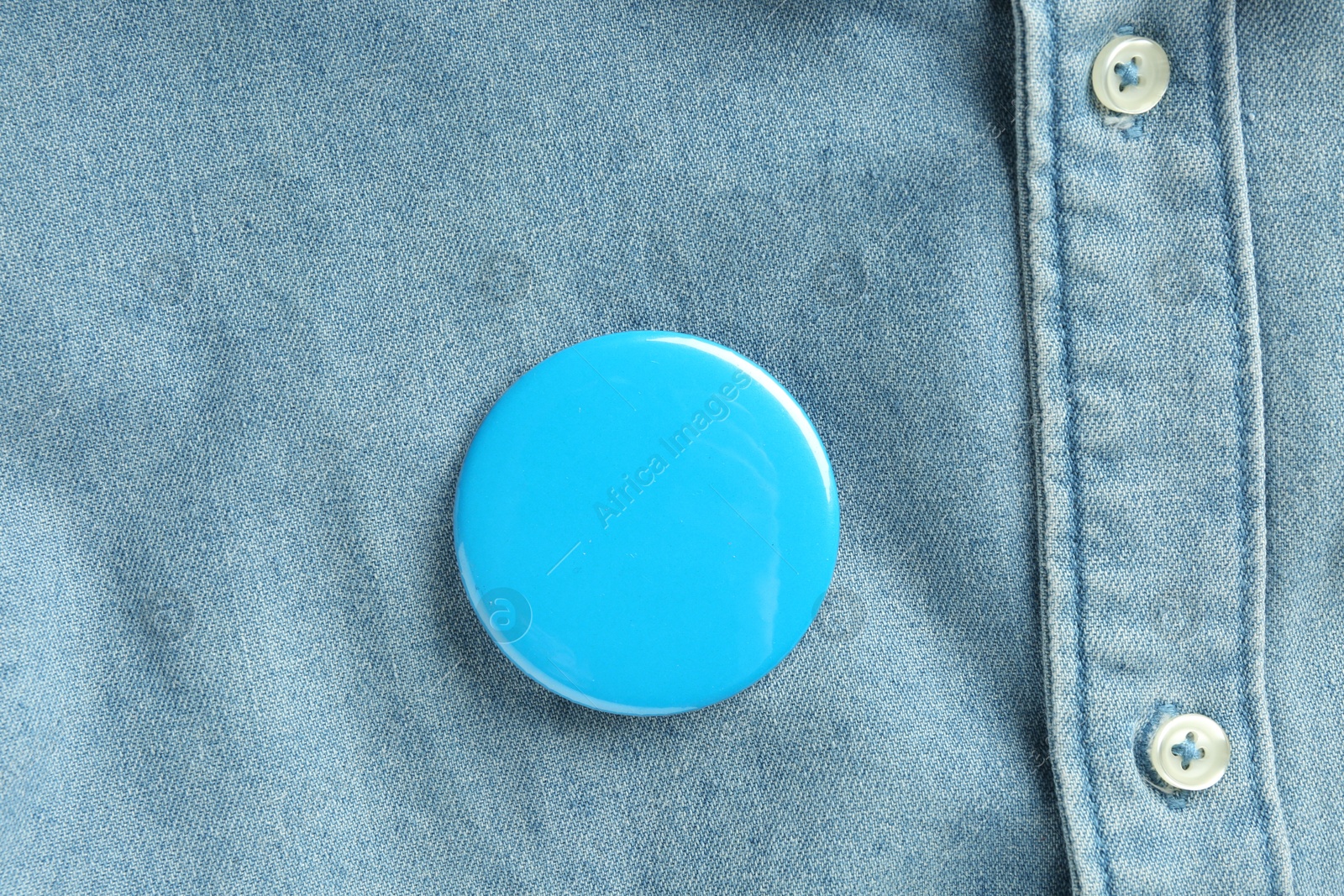 Photo of Blue button badge pinned on denim shirt, top view. Mockup for design