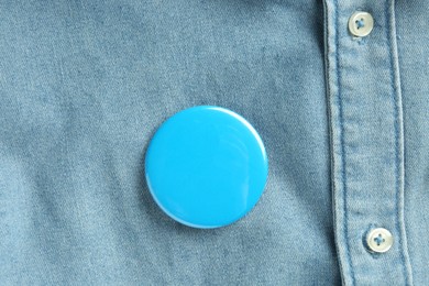 Blue button badge pinned on denim shirt, top view. Mockup for design