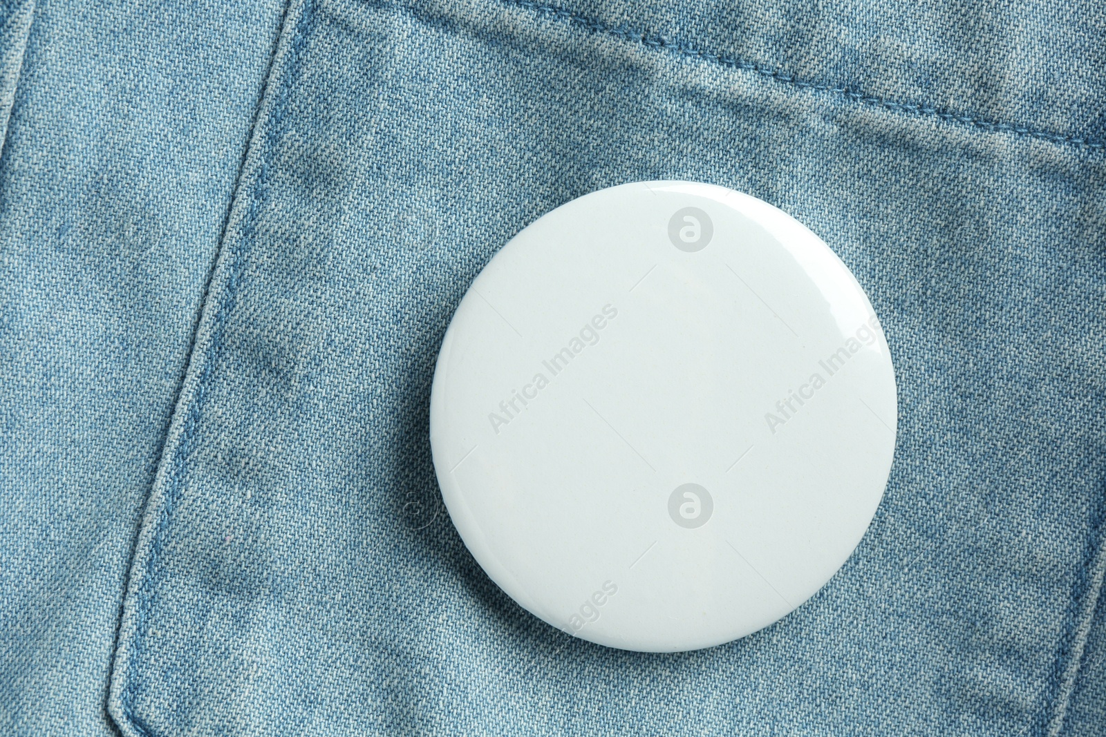 Photo of White button badge pinned on denim shirt, top view. Mockup for design