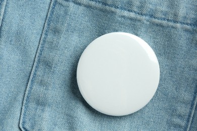 White button badge pinned on denim shirt, top view. Mockup for design