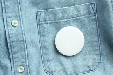 Photo of White button badge pinned on denim shirt, top view. Mockup for design