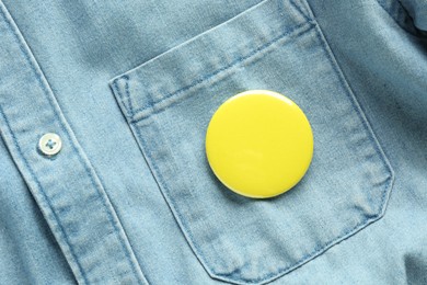 Photo of Yellow button badge pinned on denim shirt, top view. Mockup for design