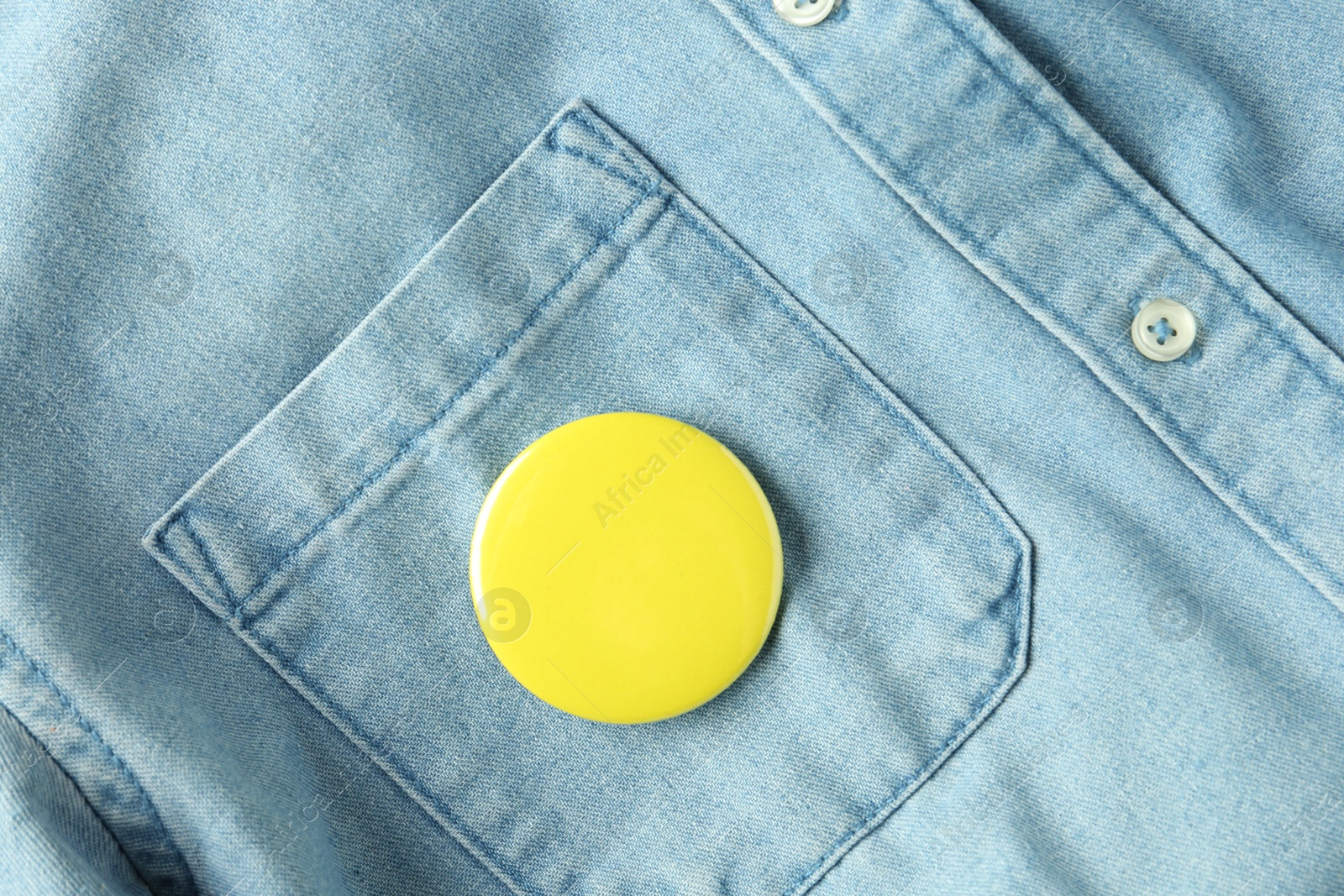 Photo of Yellow button badge pinned on denim shirt, top view. Mockup for design