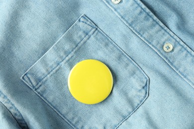 Photo of Yellow button badge pinned on denim shirt, top view. Mockup for design