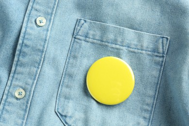 Photo of Yellow button badge pinned on denim shirt, top view. Mockup for design