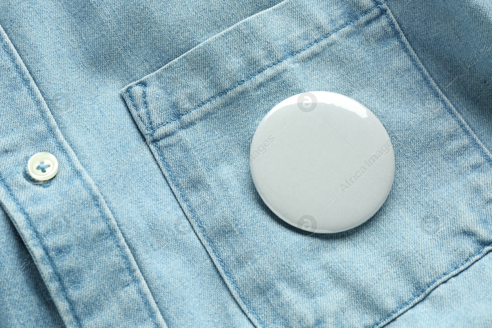 Photo of White button badge pinned on denim shirt, top view. Mockup for design