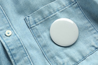 White button badge pinned on denim shirt, top view. Mockup for design