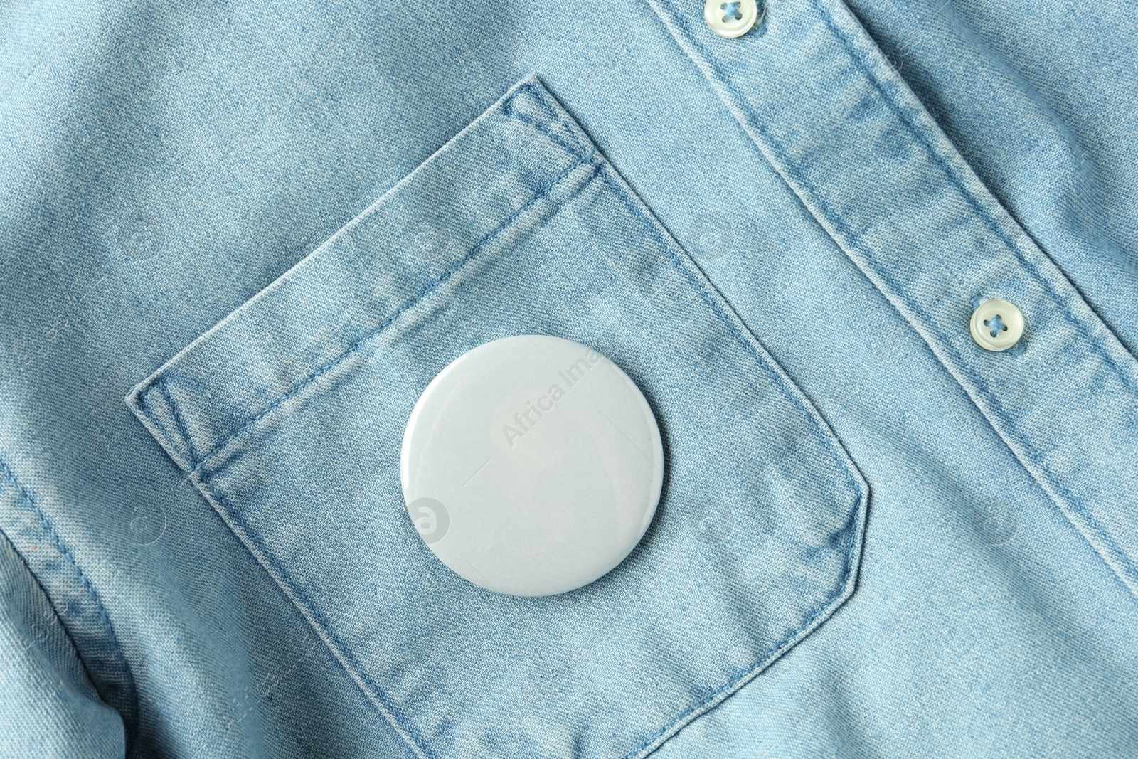 Photo of White button badge pinned on denim shirt, top view. Mockup for design