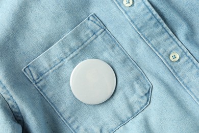 Photo of White button badge pinned on denim shirt, top view. Mockup for design