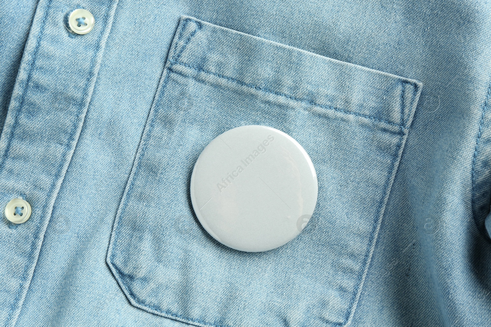 Photo of White button badge pinned on denim shirt, top view. Mockup for design