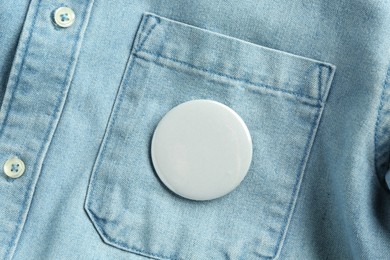 White button badge pinned on denim shirt, top view. Mockup for design