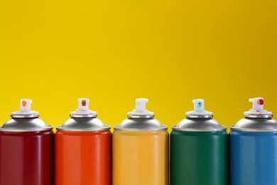 Photo of Many spray paint cans on yellow background, space for text