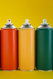 Three spray paint cans on yellow background