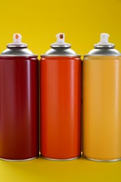 Three spray paint cans on yellow background