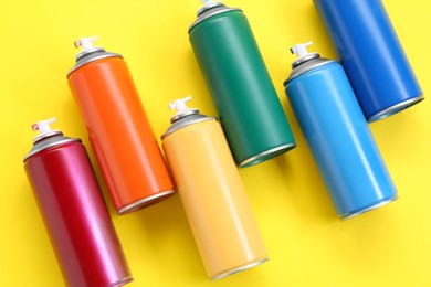 Many spray paint cans on yellow background, top view