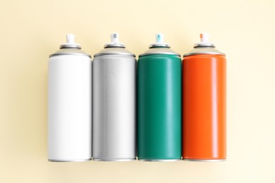 Many spray paint cans on beige background, top view