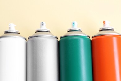 Many spray paint cans on beige background, top view