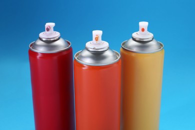 Photo of Three spray paint cans on light blue background, closeup