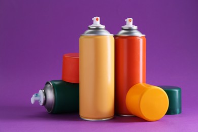 Photo of Many spray paint cans on violet background