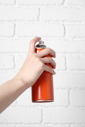 Woman with can of spray paint near white brick wall, closeup