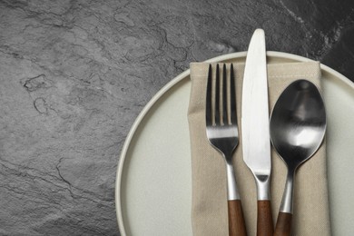 Photo of Stylish cutlery, plate and napkin on black table, top view. Space for text