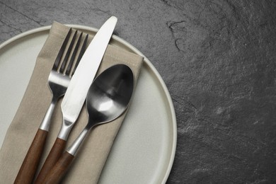 Photo of Stylish cutlery, plate and napkin on black table, top view. Space for text