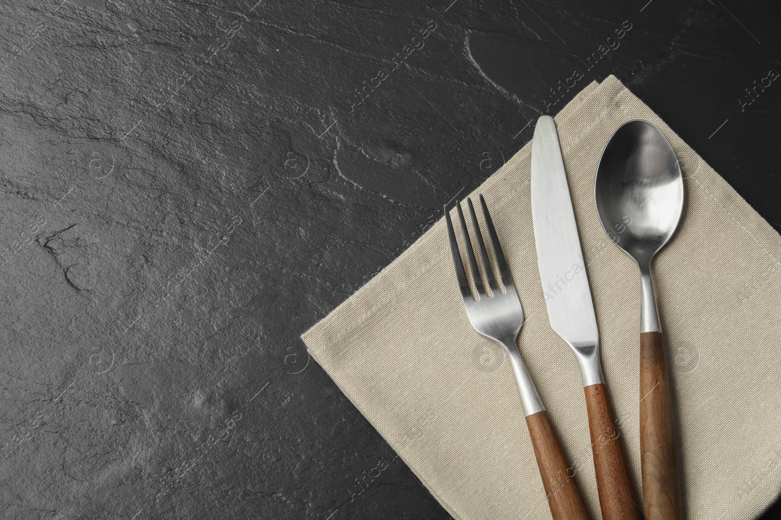 Photo of Stylish cutlery and napkin on black table, top view. Space for text