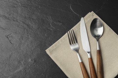 Photo of Stylish cutlery and napkin on black table, top view. Space for text