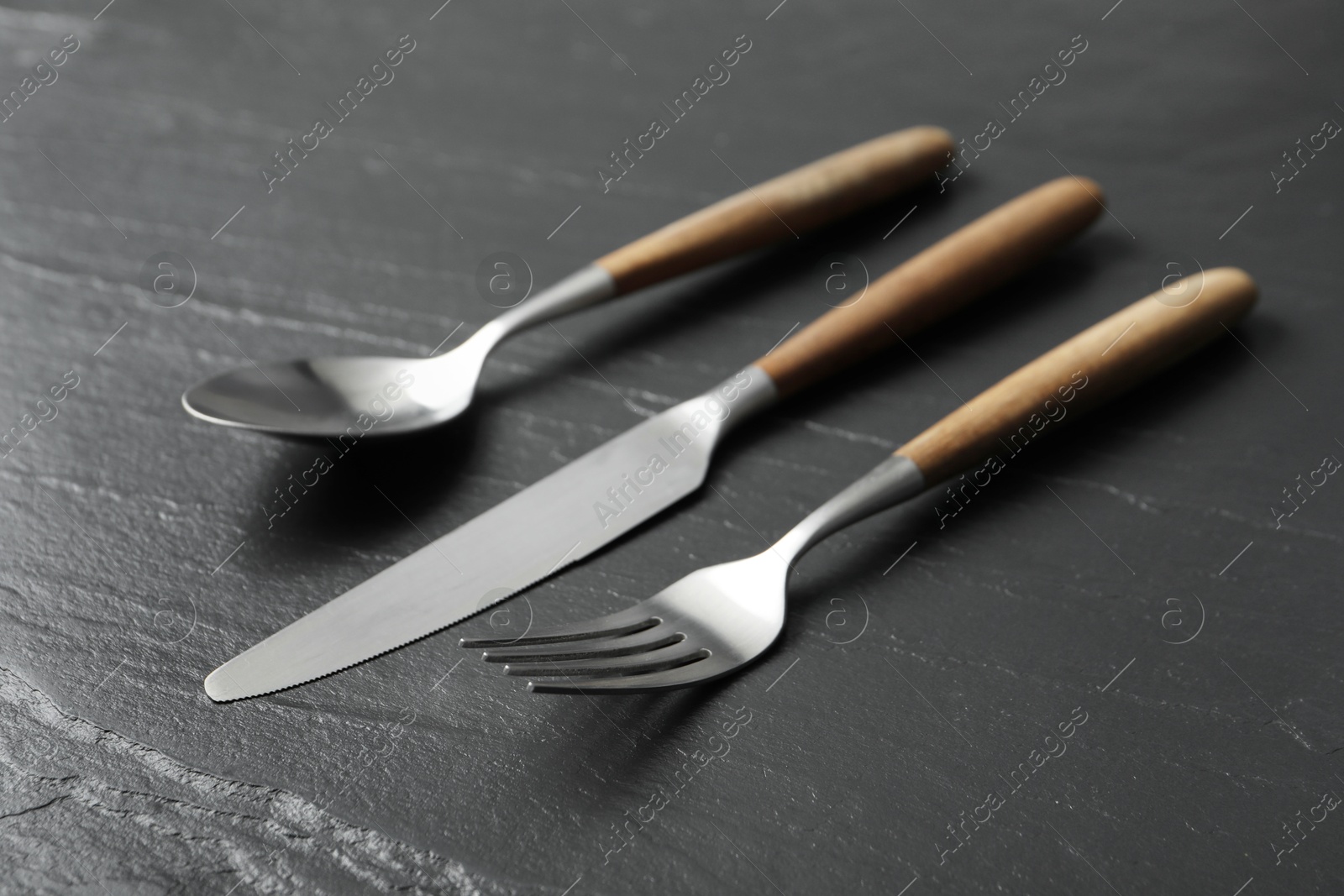 Photo of Stylish cutlery. Fork, spoon and knife on black table