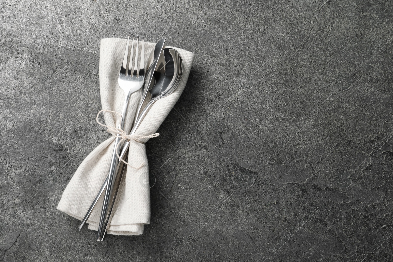 Photo of Stylish silver cutlery and napkin on grey table, top view. Space for text