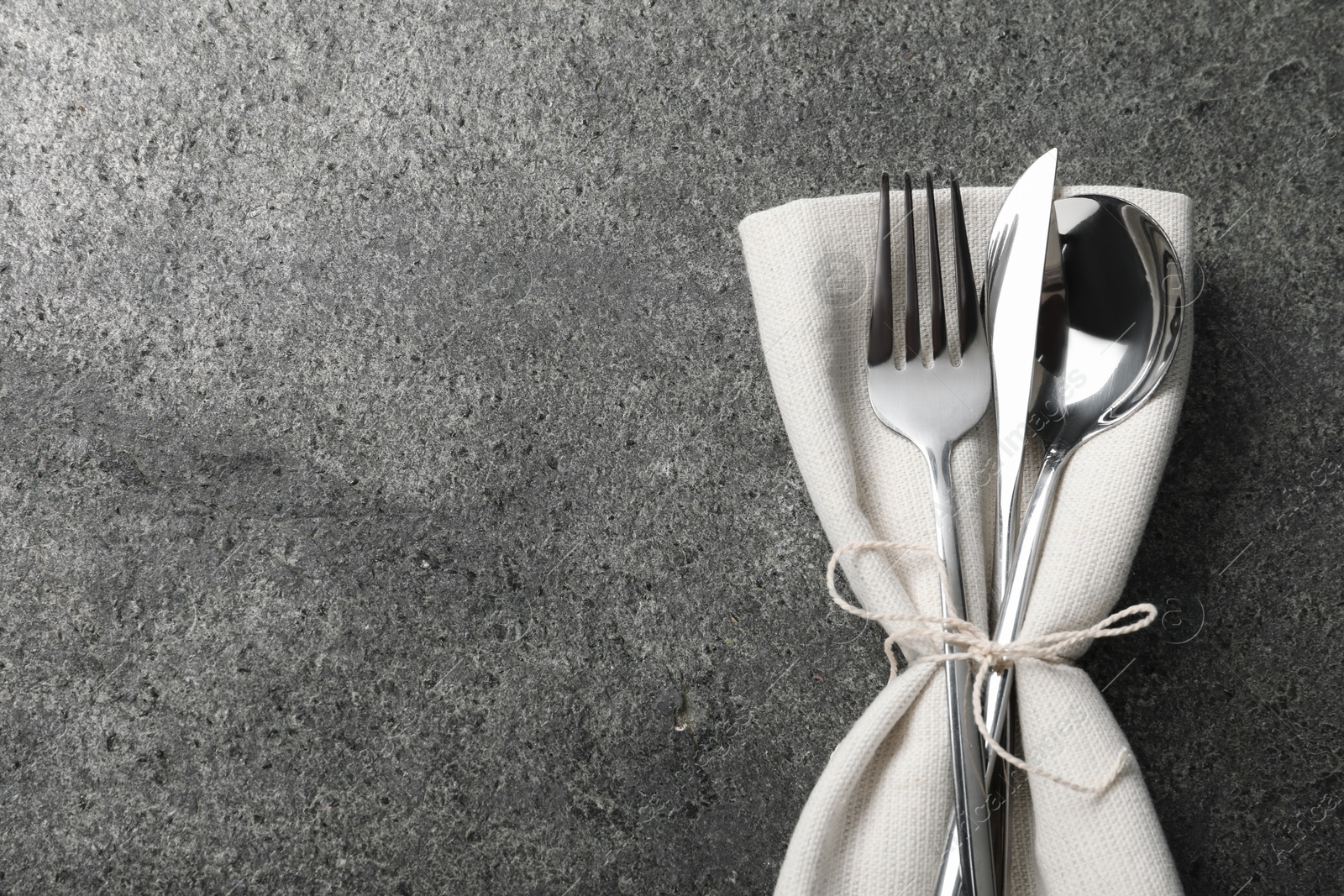 Photo of Stylish silver cutlery and napkin on grey table, top view. Space for text