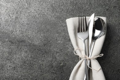 Photo of Stylish silver cutlery and napkin on grey table, top view. Space for text